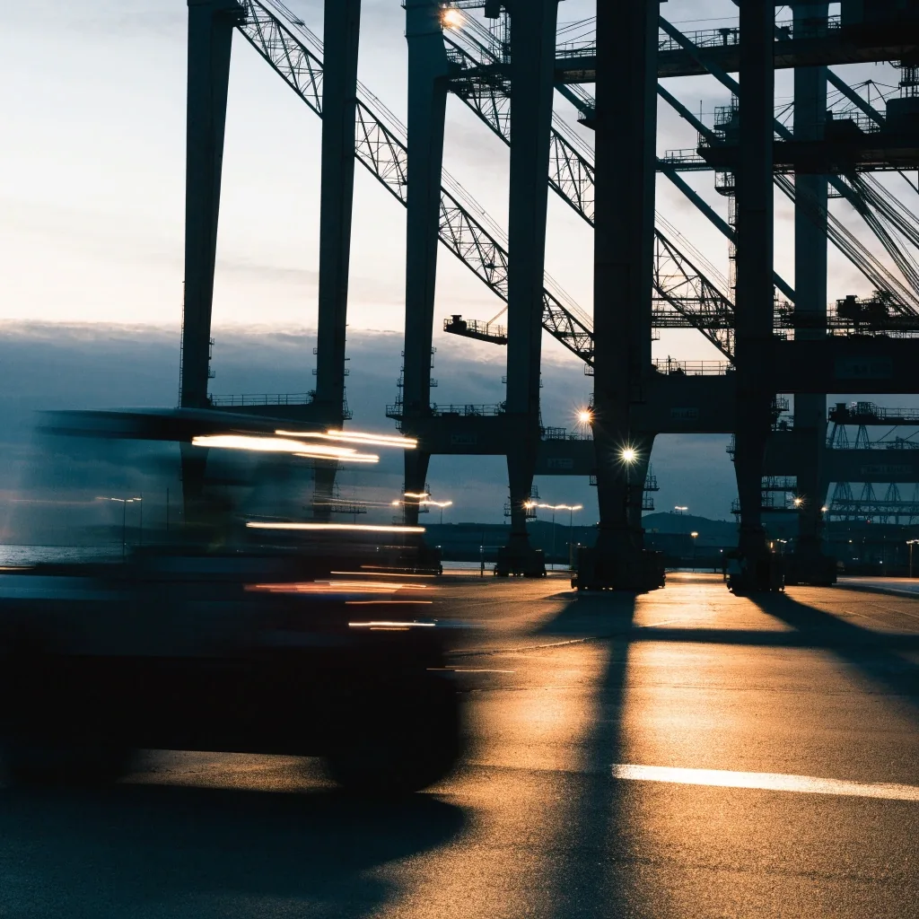 Containerbrücken im Hamburger Hafen bei Abenddämmerung, nasse Flächen mit warmen Lichtreflexen, schemenhafter Horizont